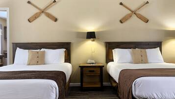 A hotel room with two beds, wooden headboards, a nightstand with a lamp, and a wall-mounted cross-shaped wooden decoration.