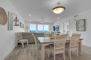 A spacious living area with a sofa, dining table, and chairs, a television, and a view of the sea. - Spectacular Gulf Front 4 bedroom/3 bath condo in the newly built Blu complex (Okaloosa Island)