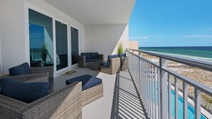 En balkon med fletmøbler, en glasdør og udsigt til strand og hav.