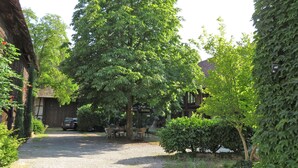 A courtyard with a gravel path, wooden furniture, and a car parked nearby. - Loft "le grenier" (Wolfgantzen)