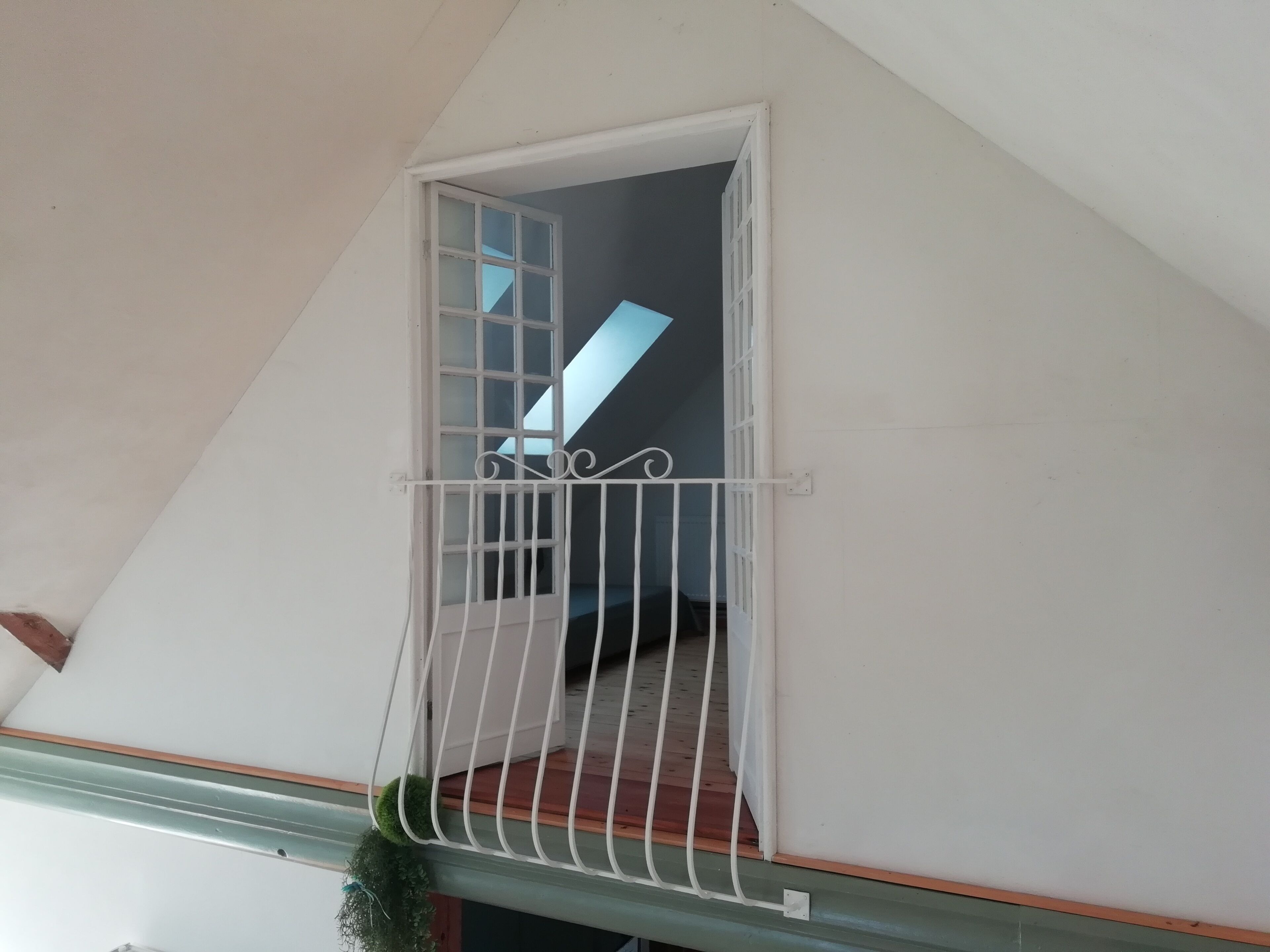 A balcony with a white metal railing, a small window, and a view of a staircase.