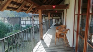 A wooden balcony with a metal railing, two wicker chairs, and a view of the garden. - Loft "le grenier" (Wolfgantzen)