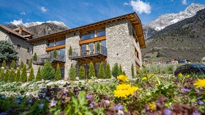 A modern two-story building with stone and wood exterior, balconies, and a mountainous backdrop.