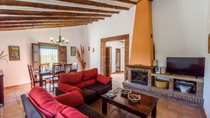 A living room with a fireplace, a television, and a dining area with wooden furniture. - Cantoblanco I Viñuela by Ruralidays (Málaga)