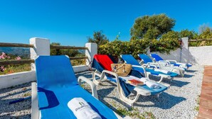 A row of sun loungers with towels and a book, set against a clear blue sky and a white wall. - Cantoblanco I Viñuela by Ruralidays (Málaga)