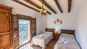 A bedroom with two beds, wooden furniture, a balcony with a view, and a chandelier. - Cantoblanco I Viñuela by Ruralidays (Málaga)