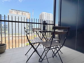 A balcony with a table and chairs, a potted plant, and a view of buildings and construction in the background.