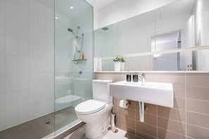 A modern bathroom with a glass shower enclosure, a white toilet, and a sink with a mirror above.