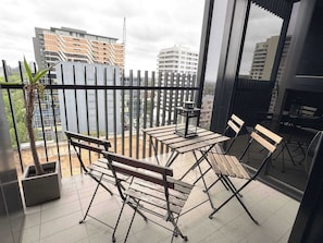 A balcony with a table, chairs, a potted plant, and a view of buildings.