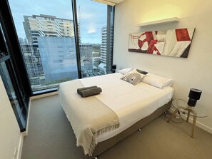 A modern bedroom with a large bed, a glass table, and a city view.
