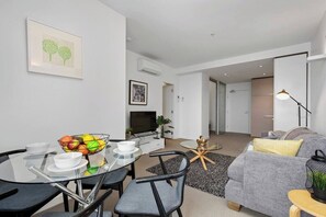 Un salon moderne avec une table à manger en verre, un canapé gris et un téléviseur.