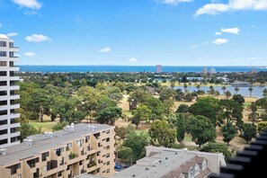 Un edificio de gran altura con varios pisos, un parque con árboles y un lago, y una vista distante del océano.