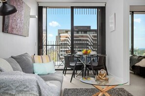 Un salon moderne avec un canapé, une table basse en verre et un balcon offrant une vue sur les immebles.