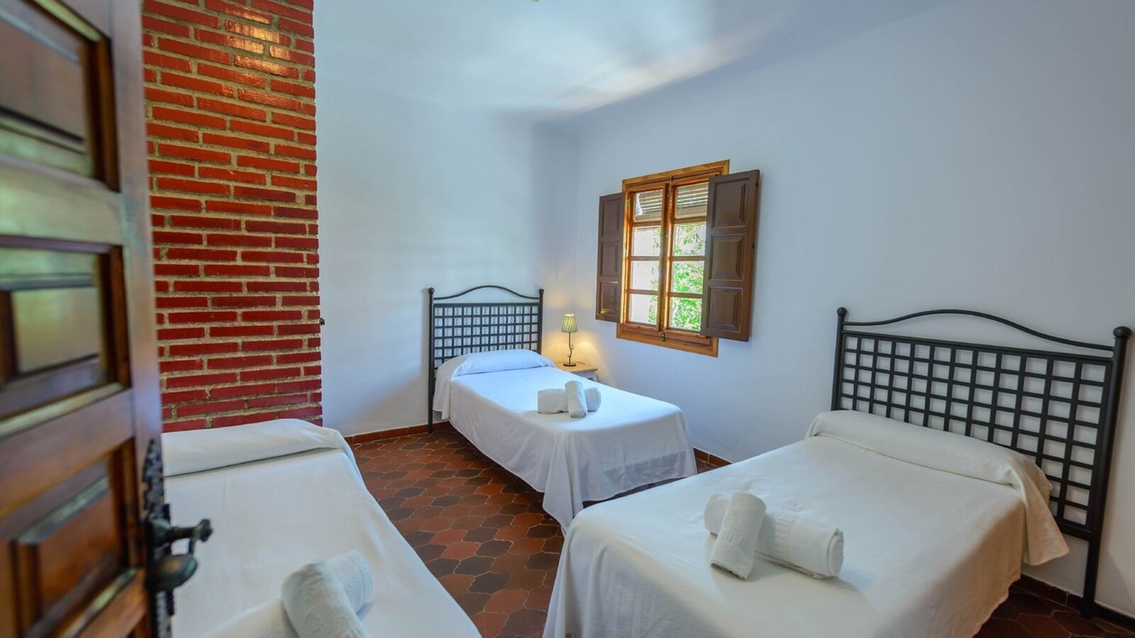 A room with two single beds, a brick wall, a window with shutters, and a door.