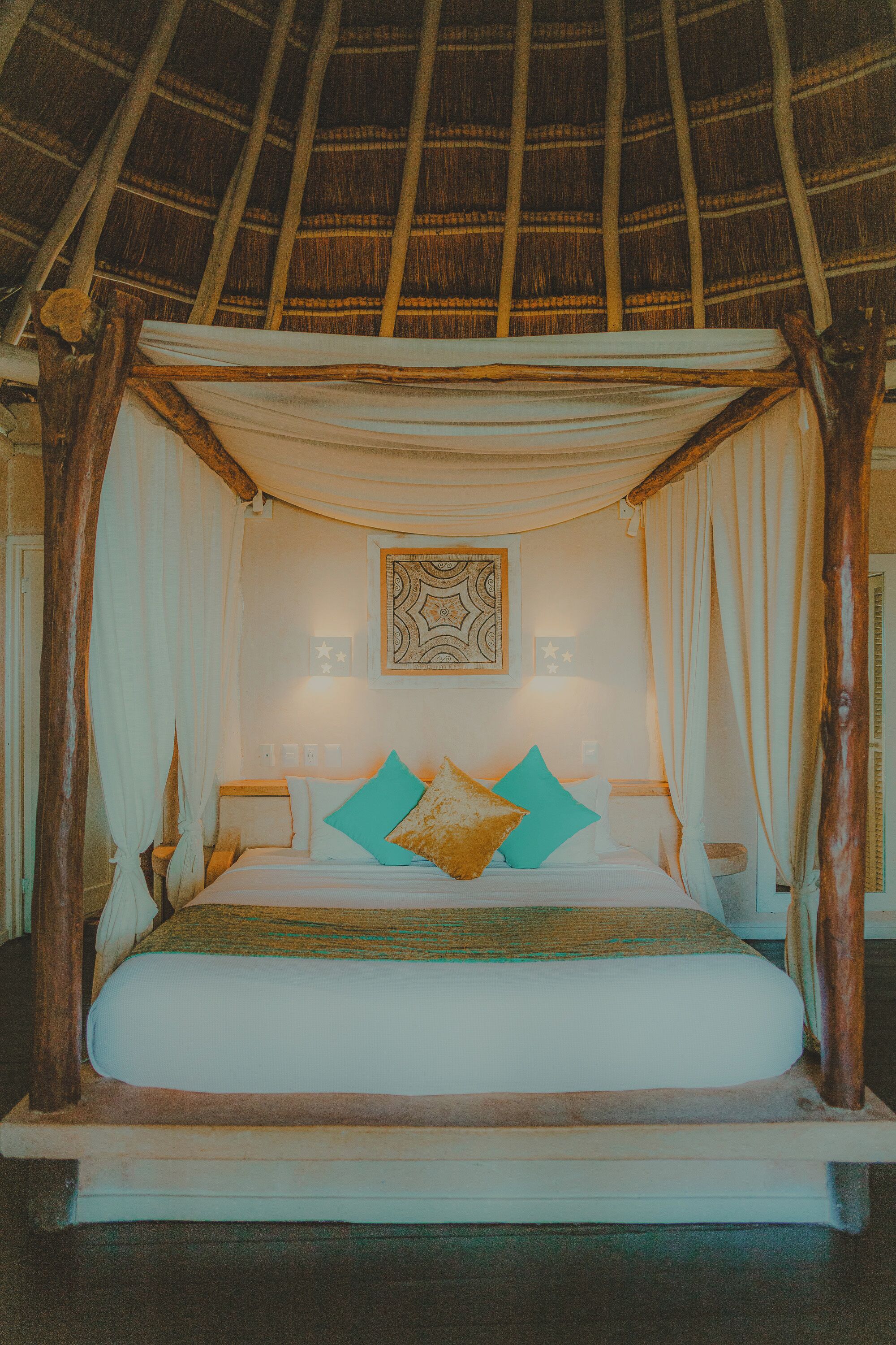 A bed with a canopy, a wall-mounted decorative piece, and a nightstand with a lamp.