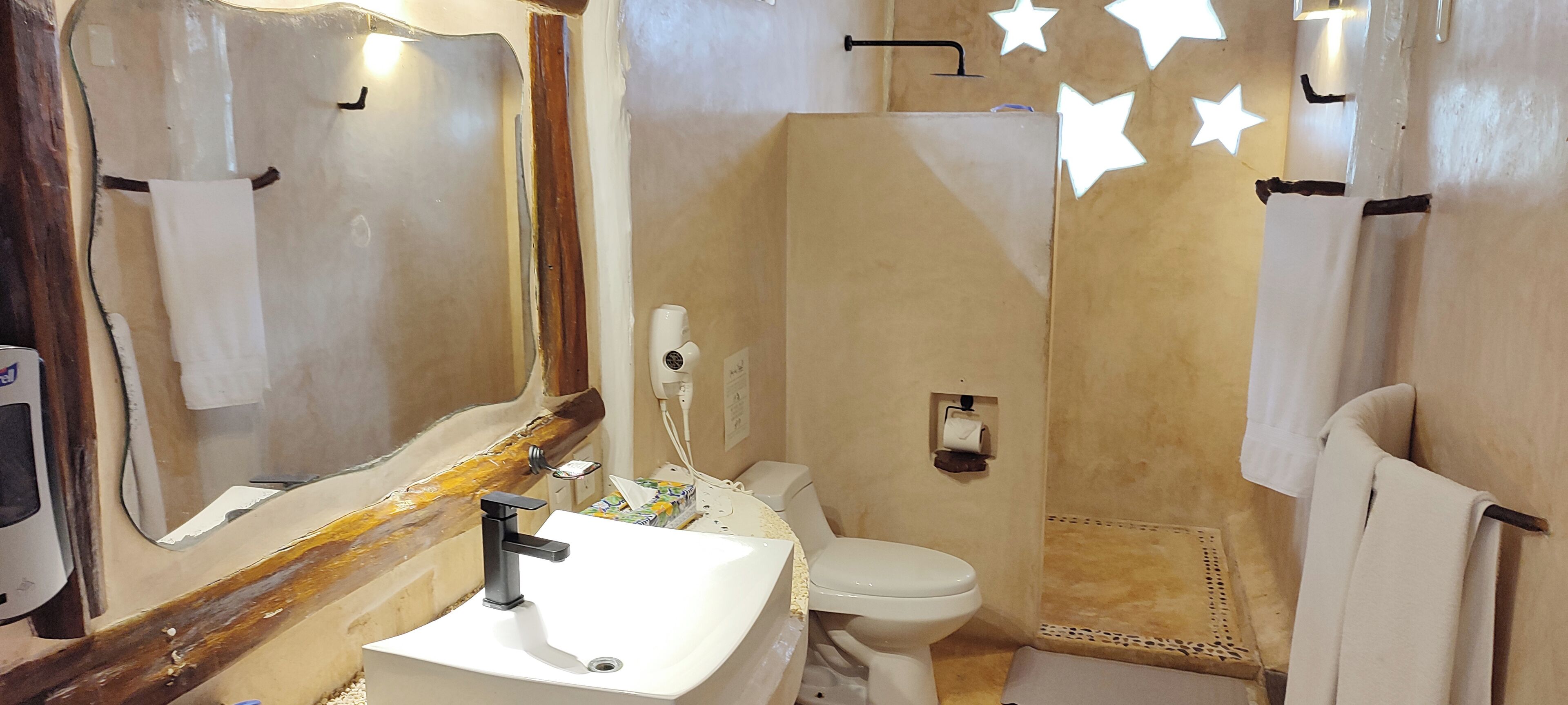 A bathroom with a sink, toilet, and mirror. There are towels hanging on the wall and a shower area.