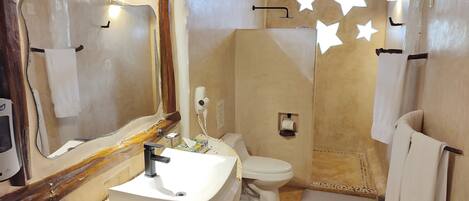 A bathroom with a sink, toilet, and mirror. There are towels hanging on the wall and a shower area.