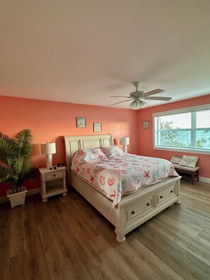 A bedroom with a bed, nightstands, a ceiling fan, a window, and a potted plant.