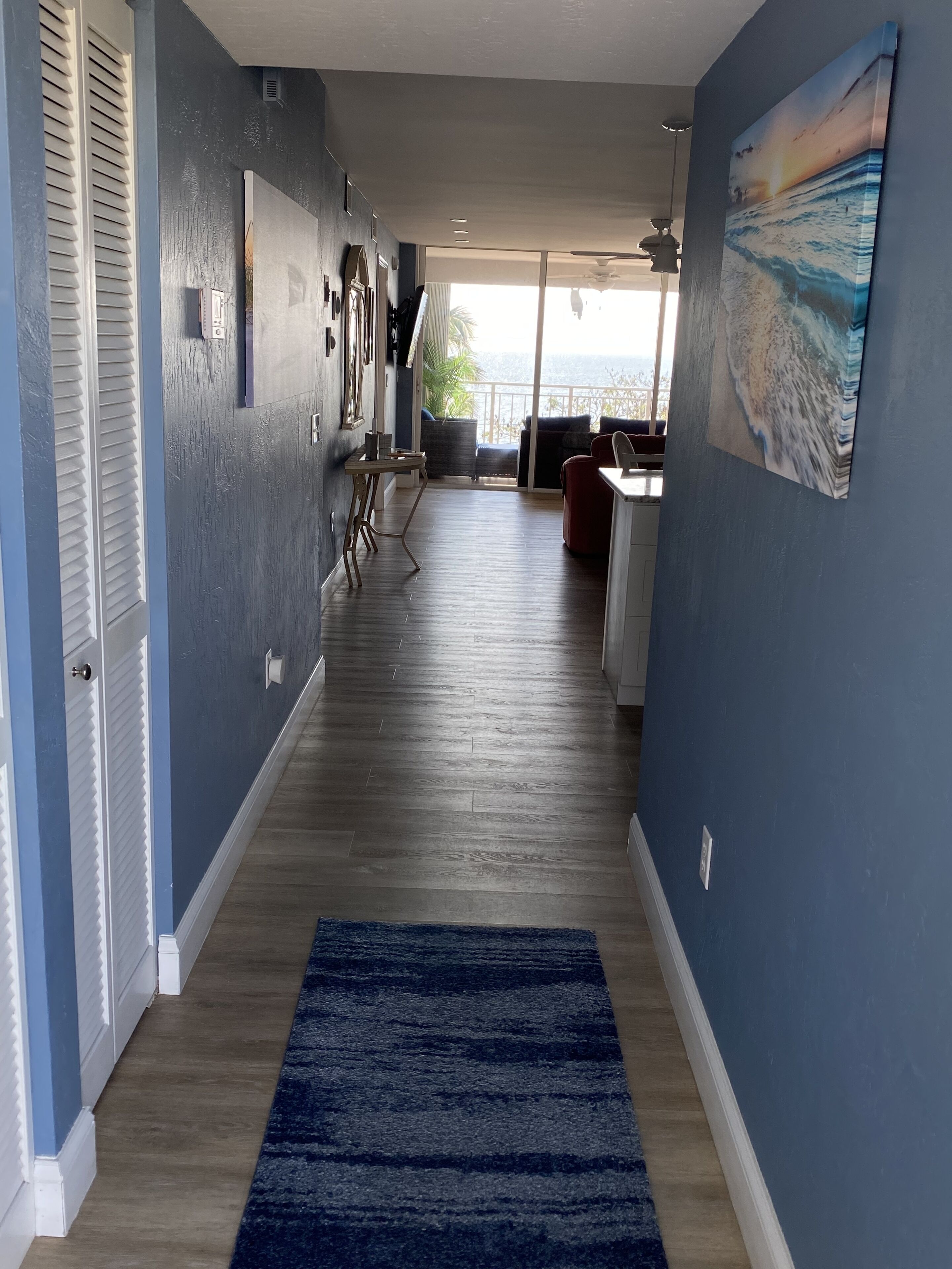 A hallway with a blue carpet leading to a balcony with a view of the ocean.