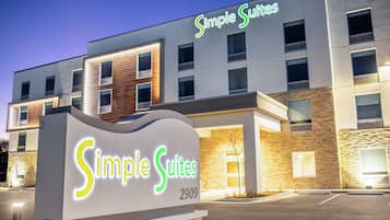 A modern hotel named Simple Suites with a signboard, a parking lot, and a well-lit facade.