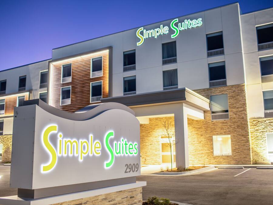 A modern hotel named Simple Suites with a signboard, a parking lot, and a well-lit facade.