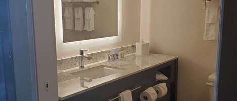 A modern bathroom with a large mirror, a sink, a toilet, and a towel rack.