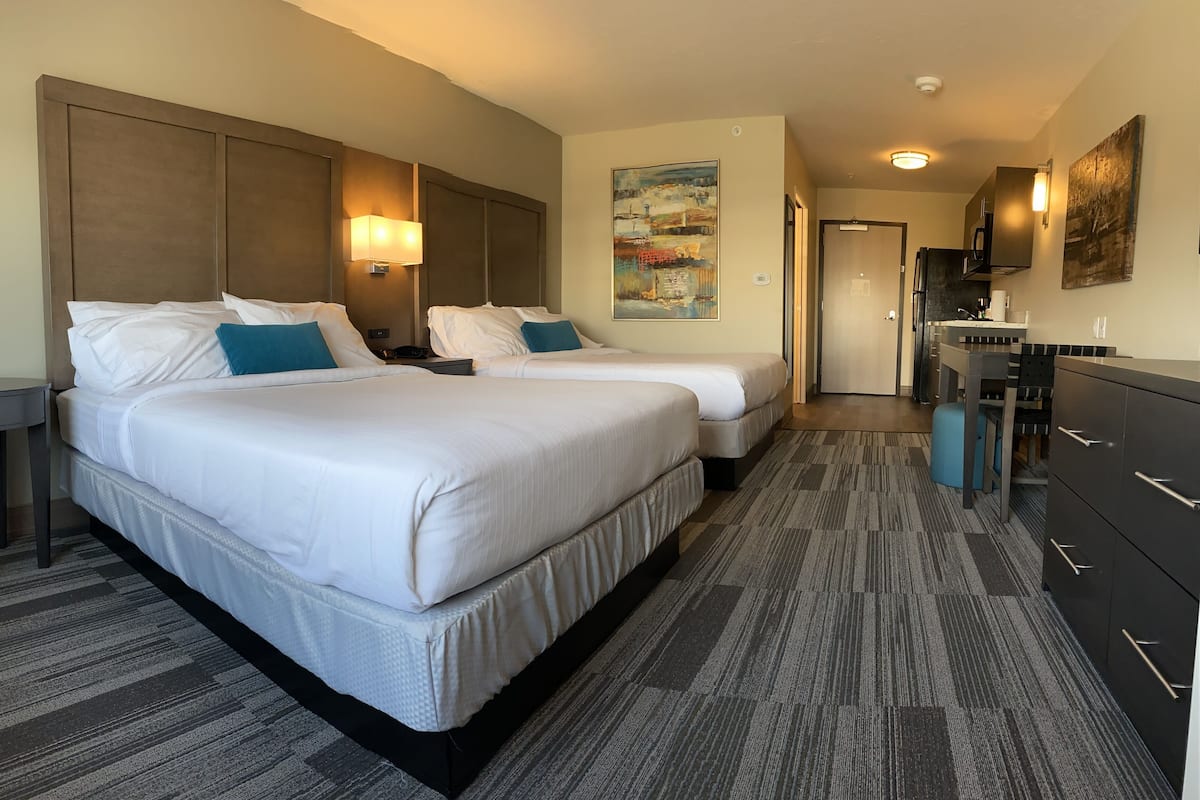 A hotel room with two beds, a desk, a chair, a dresser, and a painting on the wall.