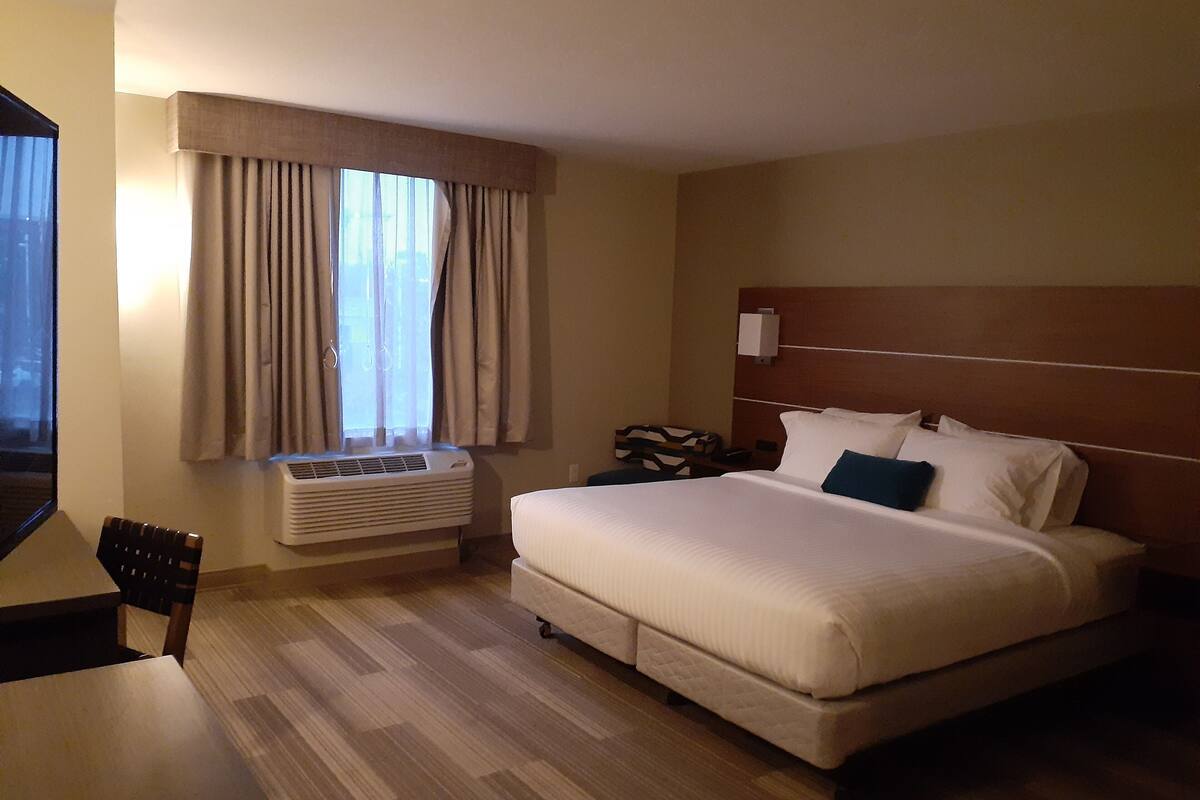 A hotel room with a large bed, a desk, and a window with curtains.