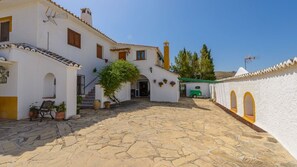 A courtyard with white buildings, stone flooring, and a green vehicle.