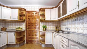 Una cucina con mobili bianchi, una porta in legno, piani di lavoro in granito e una parete rivestita con decorazioni.