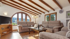 Un accogliente soggiorno con soffitto in legno, una TV, un divano, un tavolino da caffè e vista attraverso un'ampia finestra ad arco.