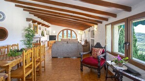 Un'ampia zona giorno con soffitto in legno, un tavolo da pranzo con sedie, un divano e un'ampia finestra con vista sull'esterno.