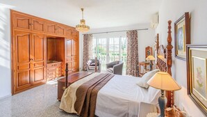 A bedroom with a large wardrobe, a bed with a headboard, a chair, a desk with a lamp, and a window with curtains. - Laurel de Mijas by Ruralidays (Málaga)