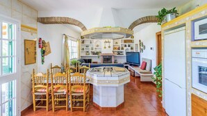 A kitchen with a central island, wooden chairs, a dining table, and a TV. - Laurel de Mijas by Ruralidays (Málaga)