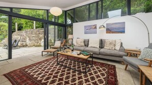 Ein modernes Wohnzimmer mit Sofa, Couchtisch und Sesseln, großen Fenstern und einer Steinsäule im Freien.