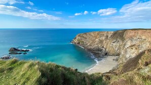 A coastal landscape with a clear blue sky, a sandy beach, and rocky cliffs. - Perfect for a romantic Cornish break and just a mile and a half from the beach. (Penwennick Road)