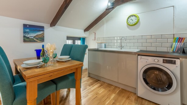 A compact kitchen with a washing machine, a dining table with chairs, and a clock on the wall. - Perfect for a romantic Cornish break and just a mile and a half from the beach. (Penwennick Road)