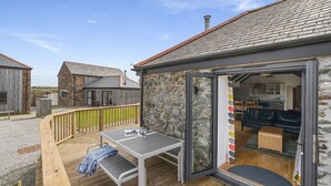 A cozy outdoor seating area with a table and benches, a stone wall, and a view into a modern kitchen.