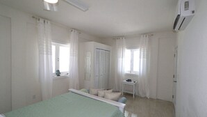 Une chambre à coucher comprenant un lit, une table de chevet, une fenêtre avec des rideaux, une armoire et un appareil de climatisation.