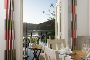 Enjoy a meal with a serene view of the lake from this dining area, featuring a table set with plates, glasses, and a vase with flowers.