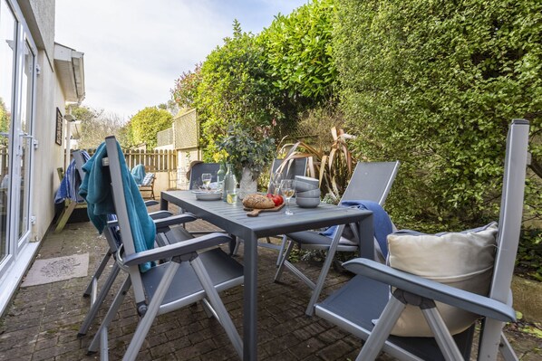 An outdoor patio with a table set for dining, surrounded by chairs and a small garden area.