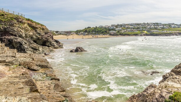Blick auf die Küste mit Felsen, einem Sandstrand und einer Wohngegend im Hintergrund.