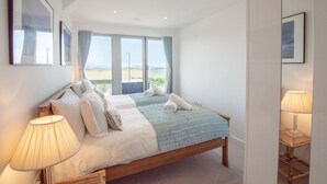 A bedroom with two beds, large windows, and a view of the beach. - A stunning first floor apartment within an award-winning development at Porth. (Newquay)