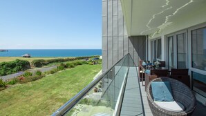 A balcony with a wicker chair and a table, overlooking a grassy area and the sea. - A stunning first floor apartment within an award-winning development at Porth. (Newquay)