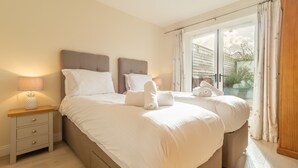 Ein Doppelbett mit weißer Bettwäsche, ein Nachttisch mit Lampe und Blick durch eine Glastür hinaus.
