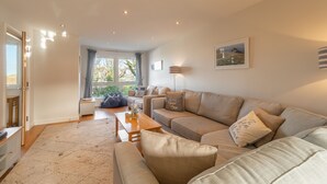 Ein modernes Wohnzimmer mit einem beigefarbenen Sofa, einem Holztisch und einem großen Fenster mit Vorhängen.
