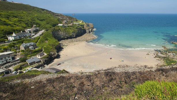 Eine Küstenlandschaft mit Sandstrand, Felsen und einigen Gebäuden.