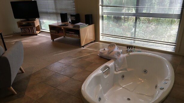 A modern bathroom with a large bathtub, a flat-screen TV, and a wooden entertainment unit.