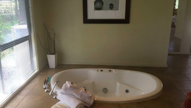 Ein modernes Badezimmer mit einer freistehenden Badewanne, einem gerahmten Kunstwerk darüber und einer Zimmerpflanze links.