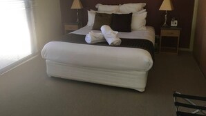 A neatly made bed with white linens and a rolled towel, two bedside lamps, and a small bedside table with a phone.